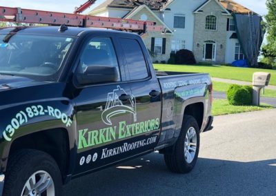 Kirkin Exteriors truck with team working on a roof replacement in the background